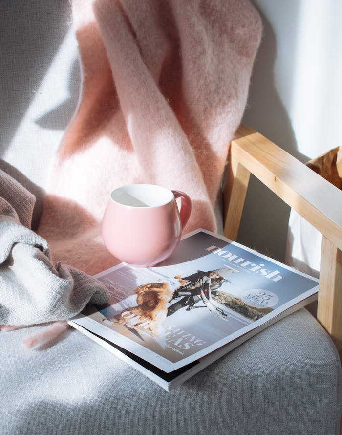 gallery-04 A warm scene featuring a pink mug and magazine on a wooden chair, bathed in sunlight.